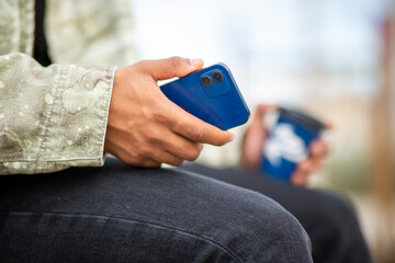 Man holding smartphone and disposable coffee cup outdoors