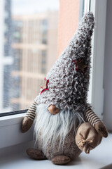 A close-up shot of a New Year's dwarf with a white beard with a bag of gifts sitting near the window.