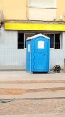 Mobile toilet positioned at a construction site near a building undergoing renovations