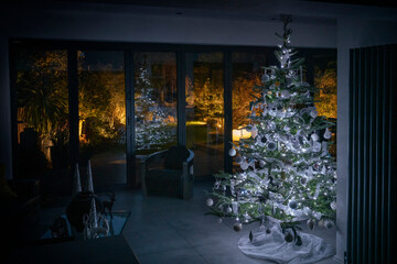 Christmas tree in darkened room with bifold doors showing a beautiful garden with garden lighting.