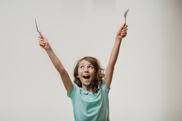 Excited girl holding fork and knife up in the air