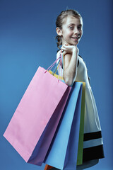 Smiling girl carrying colorful shopping bags on blue background