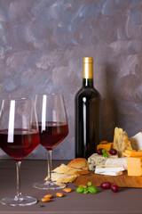 Glasses and bottle of red wine and wine appetizers cheese, bread and nuts on brown wooden background with copy space