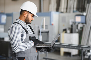 Operator of machine. Industrial worker indoors in factory. Young technician in white hard hat
