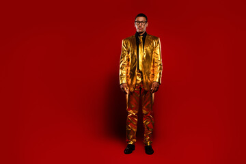 A stylish young man in a glossy golden suit stands confidently against a vibrant red background, evoking feelings of celebration