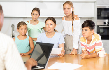 Parents with many children sit in kitchen and work with financial documents, husband enters data into electronic document on laptop