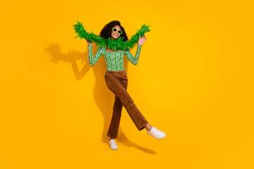 Vibrant young woman with curly hair posing playfully against a bright yellow background wearing...