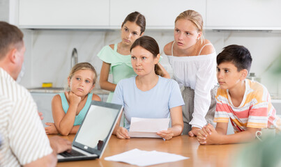 Parents with many children sit in kitchen and work with financial documents, husband enters data into electronic document on laptop