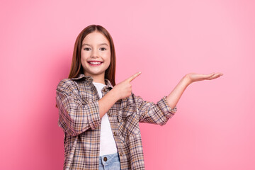 Happy young girl presenting a product on pink background, stylishly dressed in a checkered casual...