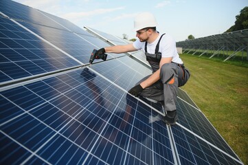 Man technician mounting photovoltaic solar moduls. Engineer in helmet installing solar panel system outdoors