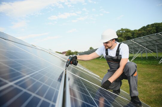 Side view of male worker installing solar modules and support structures of photovoltaic solar array. Electrician wearing safety helmet - Powered by Adobe