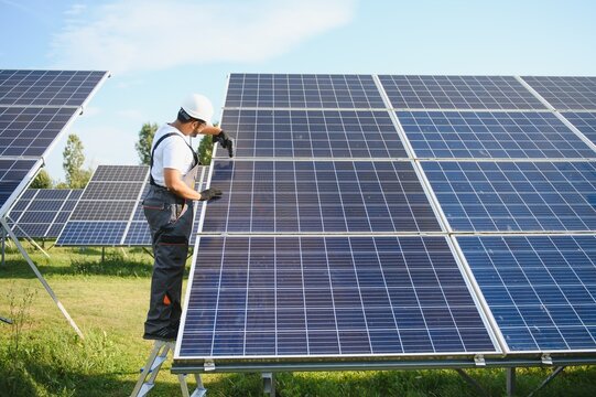 Indian man in uniform on solar farm. Competent energy engineer controlling work of photovoltaic cells