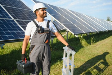 An Indian worker in uniform and with tools works on a solar panel farm