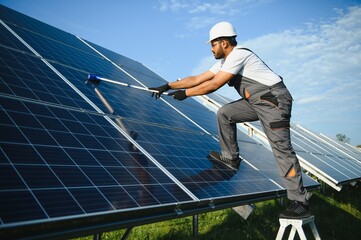 Professional indian worker cleans solar panels with brush, green electric power technology