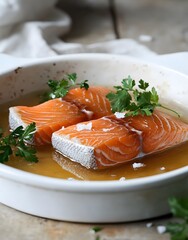 Two salmon fillets poached in a white dish with parsley and salt.