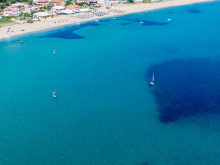 Aerial view of a tranquil beach, clear turquoise water, and sailboats. Summer vacation vibes!