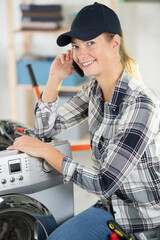 female technician talking by phone while repairing washing machine