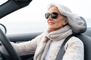 Stylish senior woman driving convertible by the sea in sunglasses and knit sweater