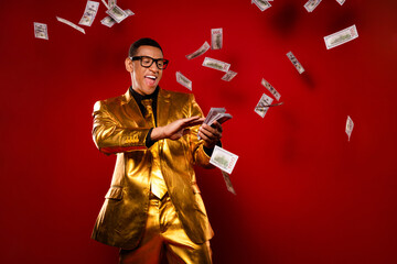Charismatic young man in a glossy gold suit joyfully tossing money against a vibrant red background