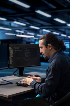 Admin typing on desktop PC in server farm establishment, ensuring data remains shielded from potential threats. IT specialist coding at computer desk, safeguarding data center against malicious access