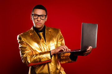 Obraz premium Elegant man in gold suit using laptop on red background, showcasing modern fashion and technology.