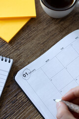 January first 2025 in a calendar notebook with sticky notes and coffee cup on wooden desk. Top view.