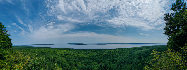 A panoramic view of a bay, islands, and lush green forest along the coast. A blue sky with clouds.