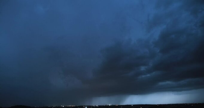 Timelapse of a heavy thunderstorm with visible curtain of falling rain and lightning strikes flashing fast as the storm cloud is slowly getting closer to the camera and more intense