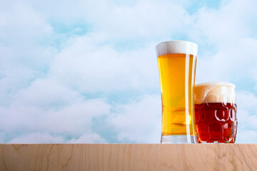 Modern Yellow Blonde and Old Fashioned Amber Ale Craft Brewed Beer Drinks with Large Foam Heads and Cloudy Blue Sky Backdrop