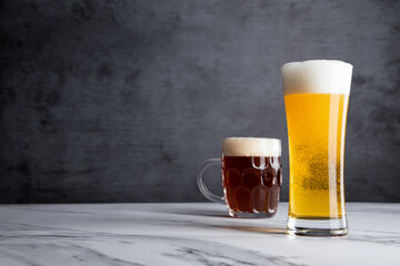 Two Glasses of Golden Yellow Blonde and Amber Ale Beer Drinks with Large Delicious Foam Heads and a Gray Backdrop