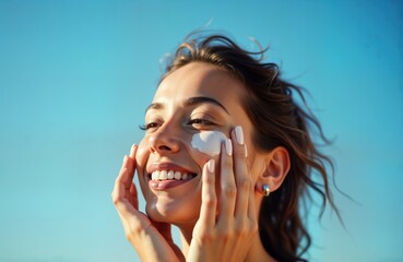 Young woman applies sunscreen on face under bright blue sky. Looks happy, healthy. Photo about skin protection during sunny days. Shows skincare routine in summer lifestyle. Daily essential important