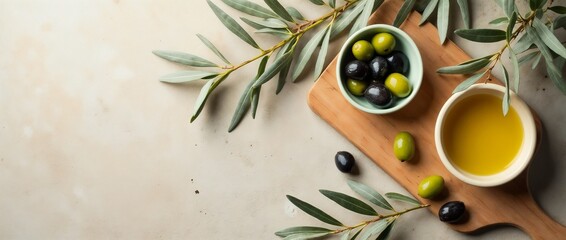 High-angle view of a ceramic bowl containing fresh green and black olives, a cup of olive oil, and an olive branch on a cutting board.

