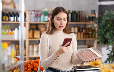 Young female shopper scanning qr code for packaged raw sausages in grocery store