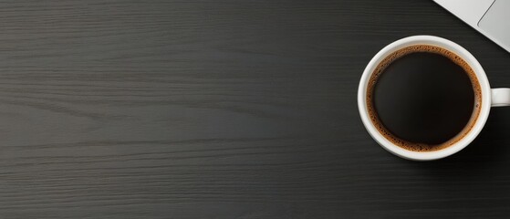 Hot black coffee rests on a dark wooden table next to a notebook for easy access during work
