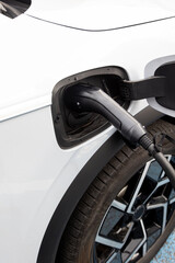 Close-up of an electric vehicle being charged. The white car is connected to a charging station via a black cable, highlighting eco-friendly transportation trends.