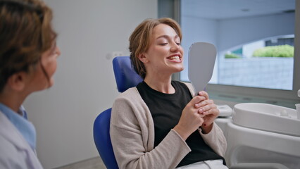 Dentistry patient looking mirror with happy expression at dental checkup closeup