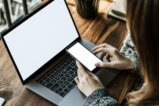 Caucasian woman holding white blank smartphone and laptop mockup, home office concept
