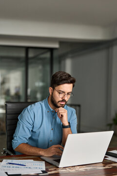 Busy professional business man employee, young businessman software engineer looking at computer thinking on online investment analysing market using laptop working at office, vertical photo.