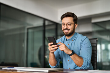 Busy young Latin business man holding smartphone working in office. Professional happy businessman...