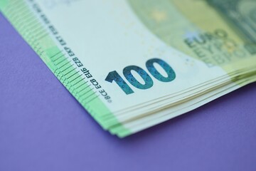 Big amount of one hundred euro money bills on lilac background