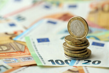 One euro coin lies on huge amount of different euro dollars banknotes