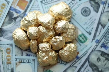 Small pile of golden nuggets and big amount of hundred US dollar bills