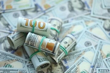 Many rolls of one hundred dollar bills lies on big amount of american currency banknotes