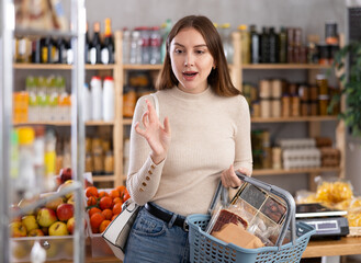Young woman buyer with basket of food buying products in grocery store