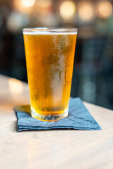 A clear pint drinking glass filled with cold foam from a lager ale. The Irish red ale pint sits on the edge of a metal patio table at a microbrewery. The background is lighter and out of focus.