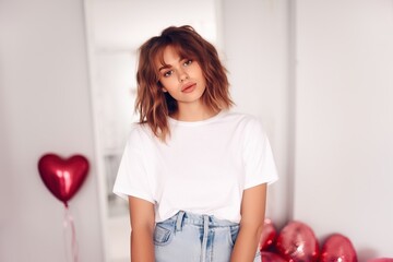 Young girl dressed in white T-shirt for the mockup and stay in the room decorated with balloons for St. Valentine's Day.