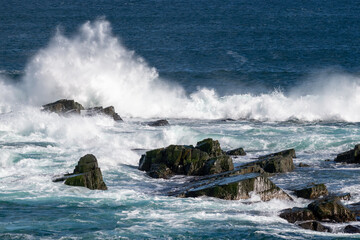 An angry turquoise green color massive rip curl of a wave as it rolls along a beach. The white mist and froth from the wave are foamy and fluffy. The Atlantic Ocean in the background is deep blue. 