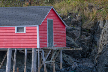 A vintage wooden fishing shed on stilts built into a rocky coastline over water. The fishing stage...