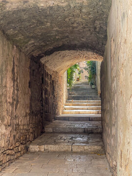 Korcula, Croatia - June 30, 2024: Look into alley with mostly steps and part under buildings. Green foliage in backj