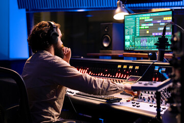 Audio expert operating on control desk with motorized faders and mixing console in professional studio, using sliders and knobs to process sounds. Music engineer producer recording tracks.